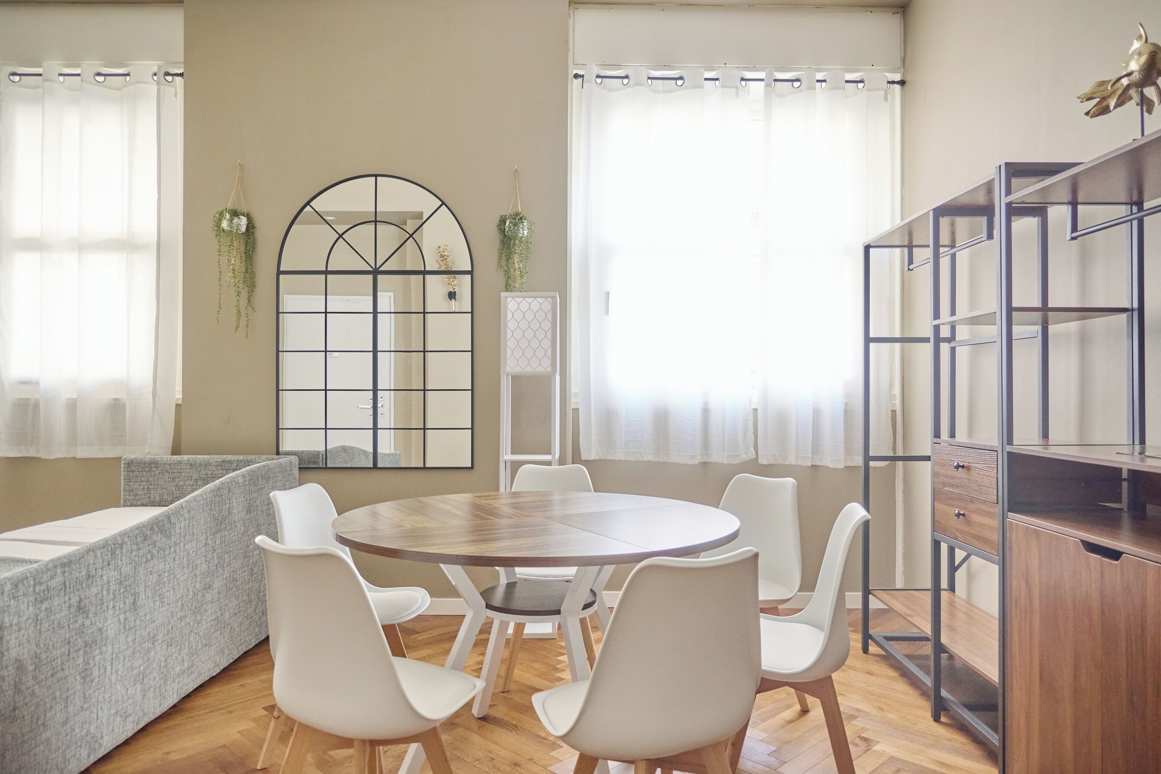 A modern dining area with a round wooden table and white chairs, a built-in bookshelf, and a decorative window with a geometric design.