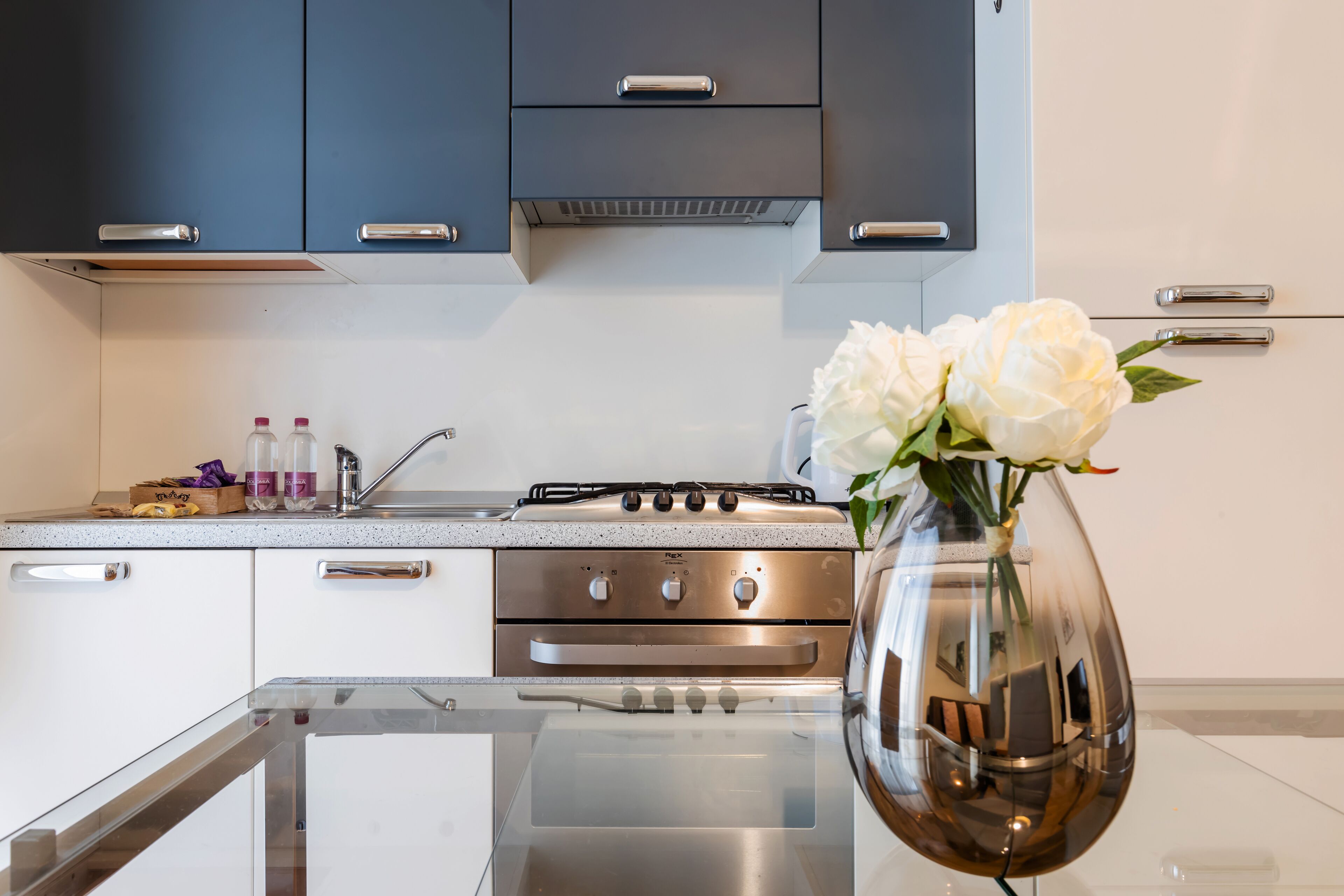 A modern kitchen with stainless steel appliances, a glass countertop, and a vase with flowers on the island.