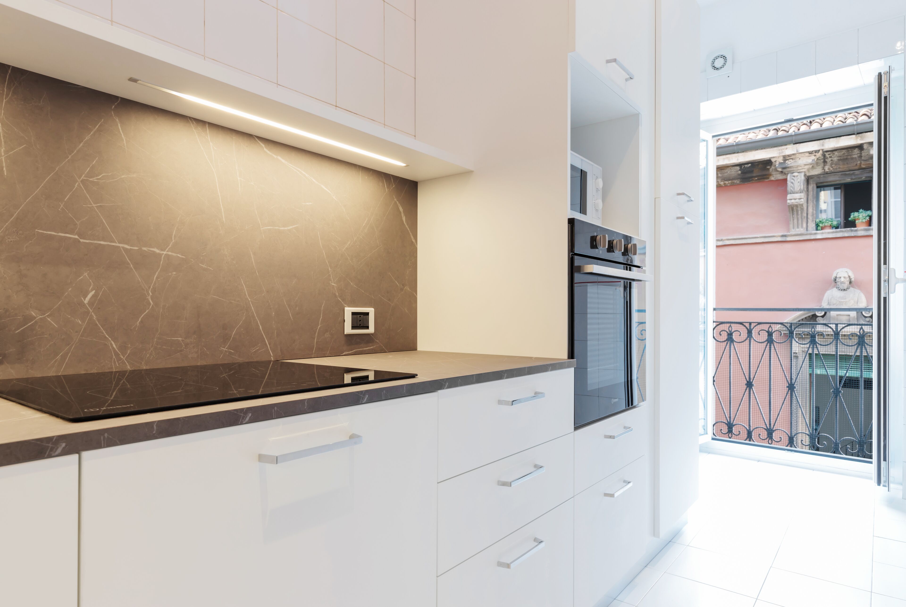 Una cocina moderna con armarios blancos, encimera negra y horno empotrado.