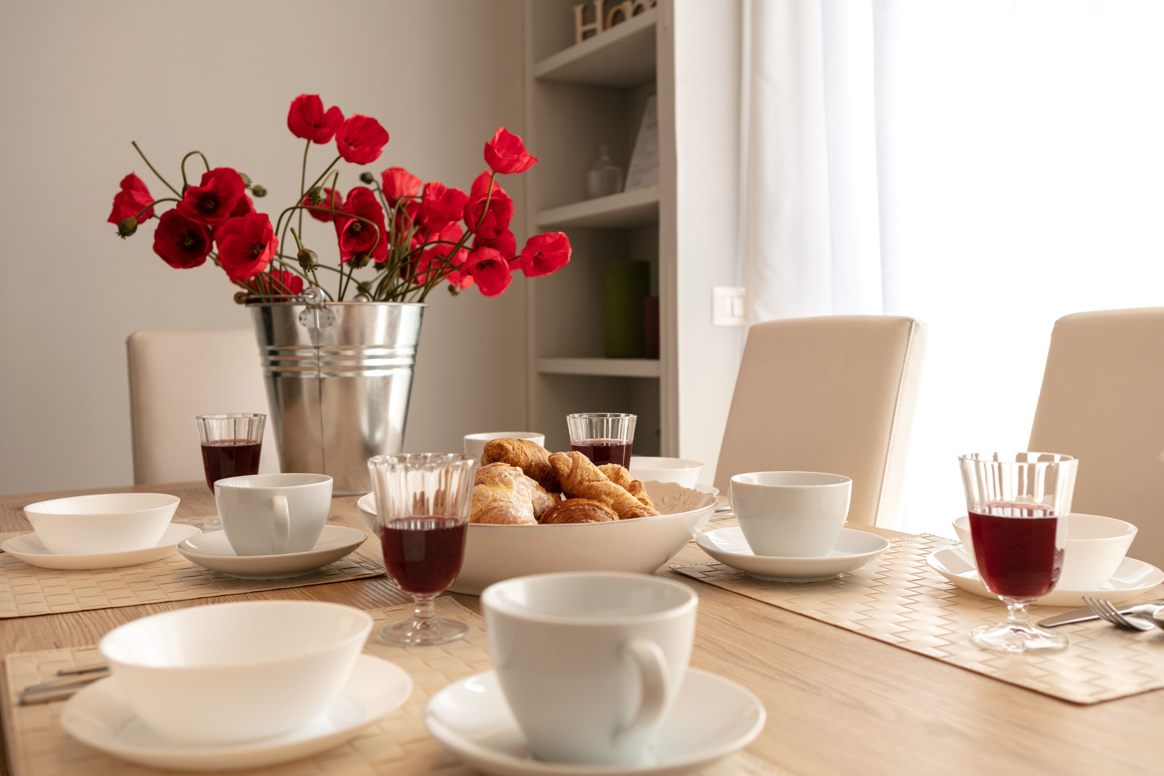 A dining table with white bowls, cups, and a vase of red flowers.