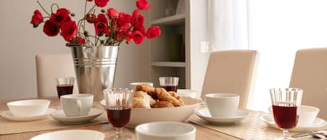Una mesa de comedor con cuencos blancos, tazas y un jarrón de flores rojas.