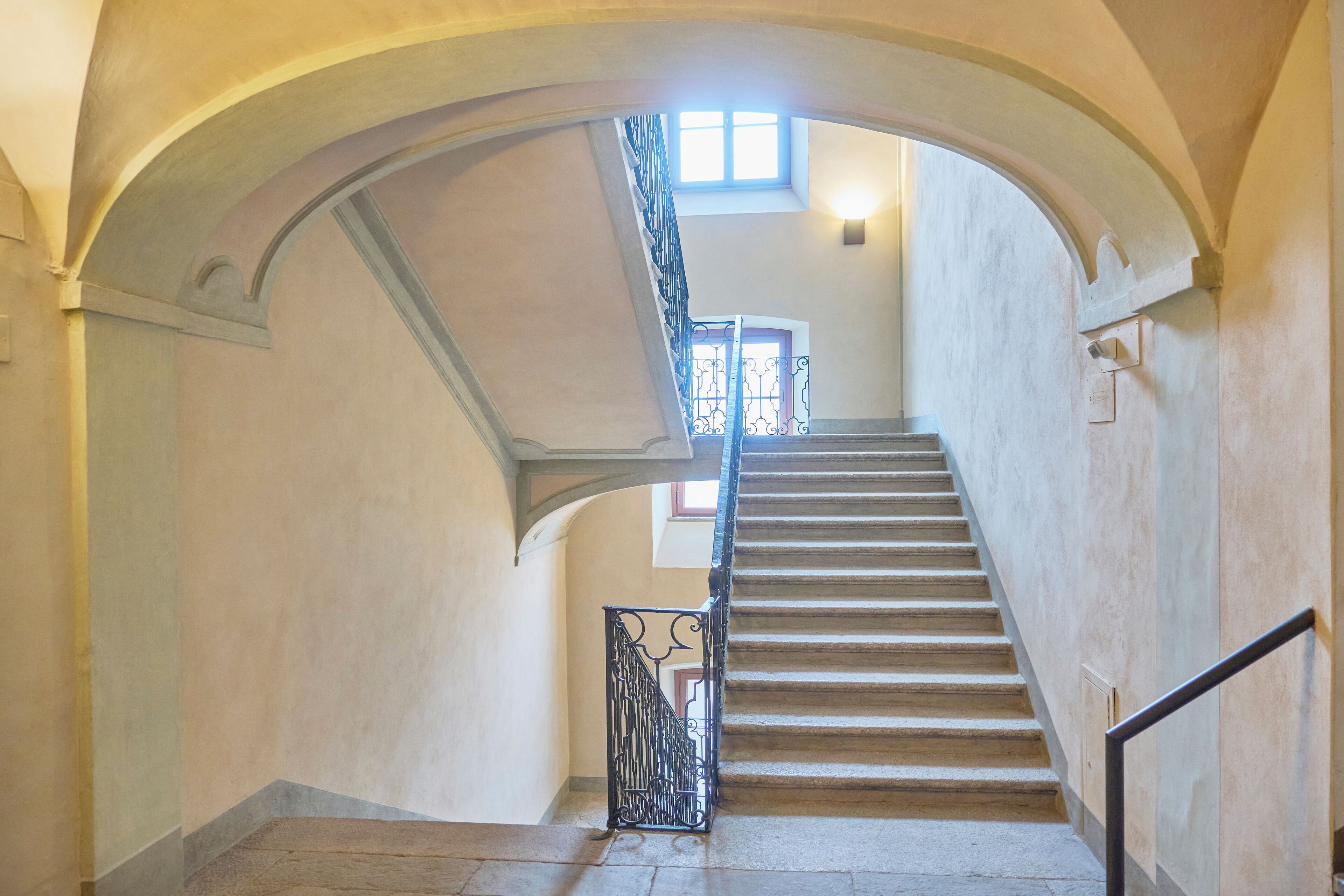 A grand staircase with a wrought iron railing, leading to a landing with a door and a window above.