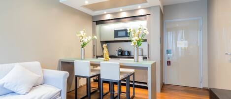 Una sala de estar moderna con un sofá blanco, una mesa de comedor con sillas, una zona de cocina con microondas y una puerta con un cartel.