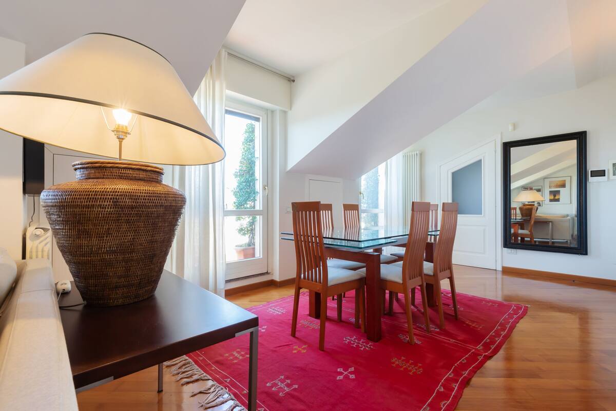 A dining area with a table, chairs, a lamp, and a red rug.