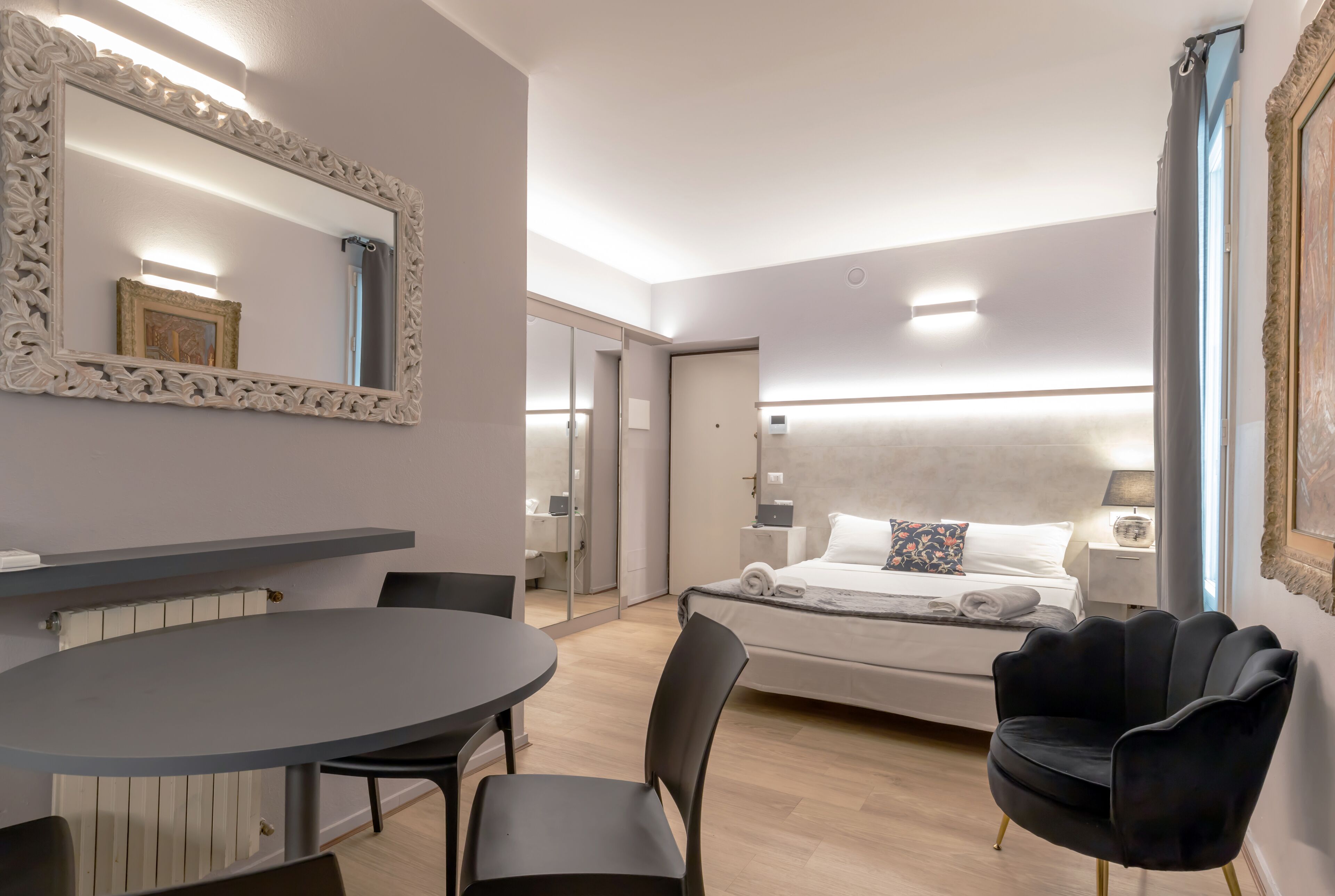 A modern hotel room with a large bed, a round dining table, and a black chair.