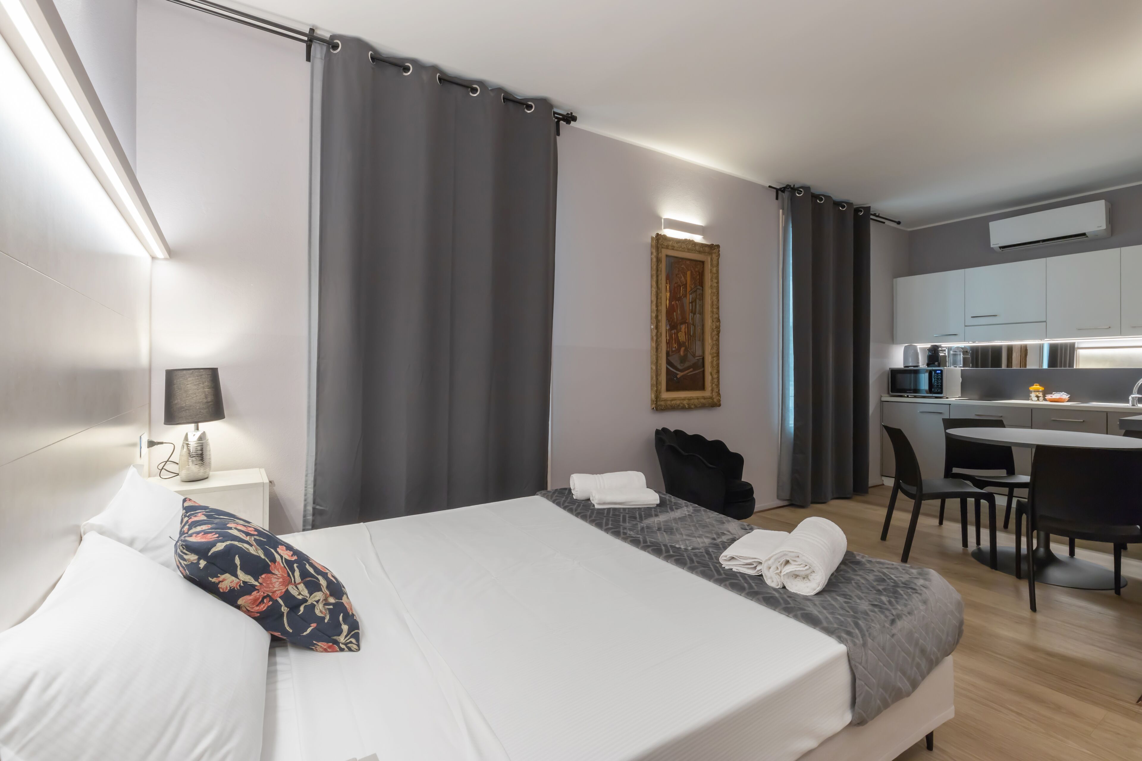A modern hotel room with a neatly made bed, a small desk, and a kitchenette.