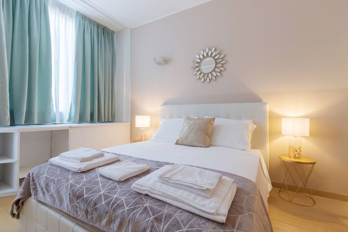 A neatly made bed with folded towels, a bedside lamp, and a decorative mirror on the wall.