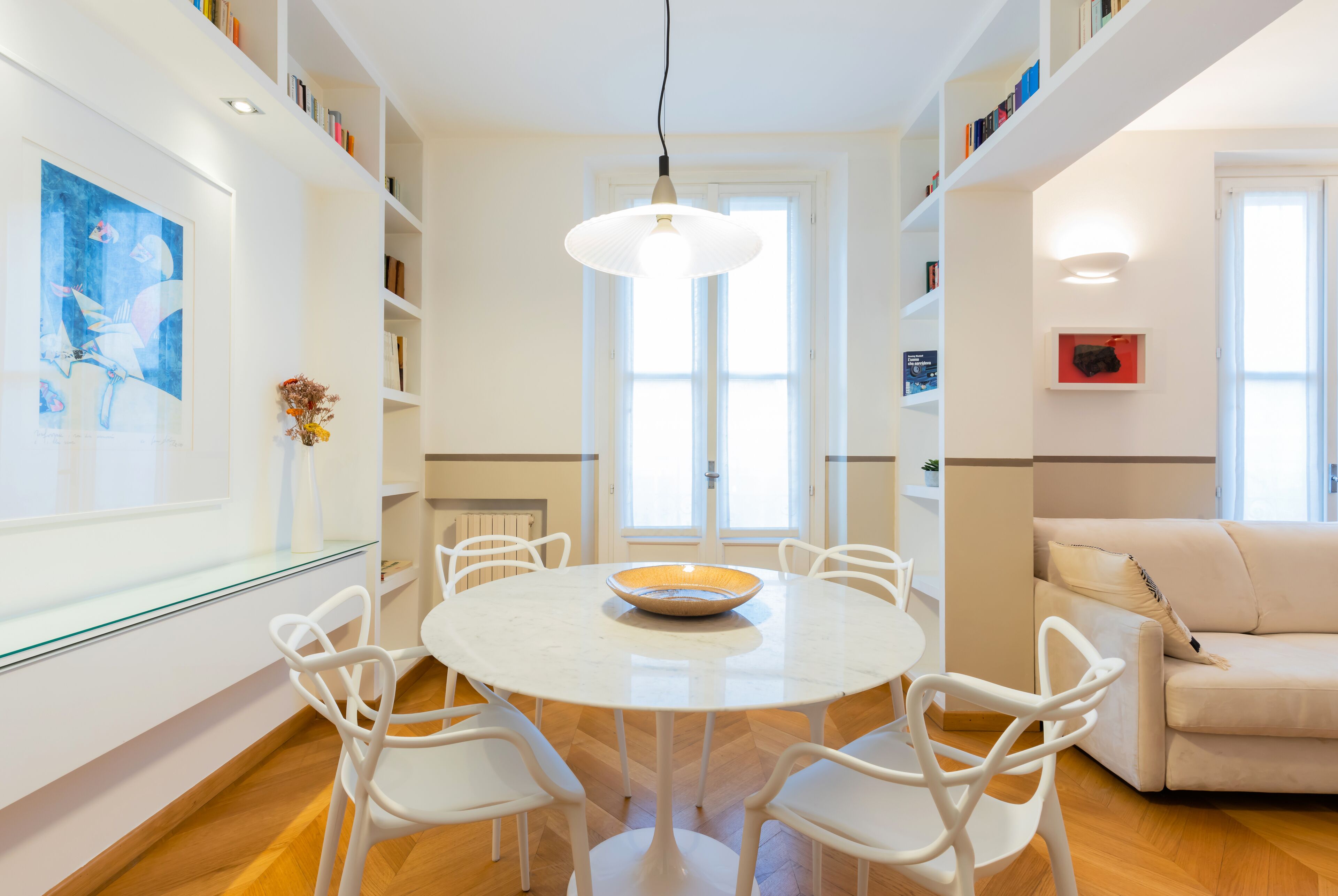 Ein modernes Wohnzimmer mit einem runden weißen Tisch, weißen Stühlen, einem beigen Sofa und einem Glastisch.