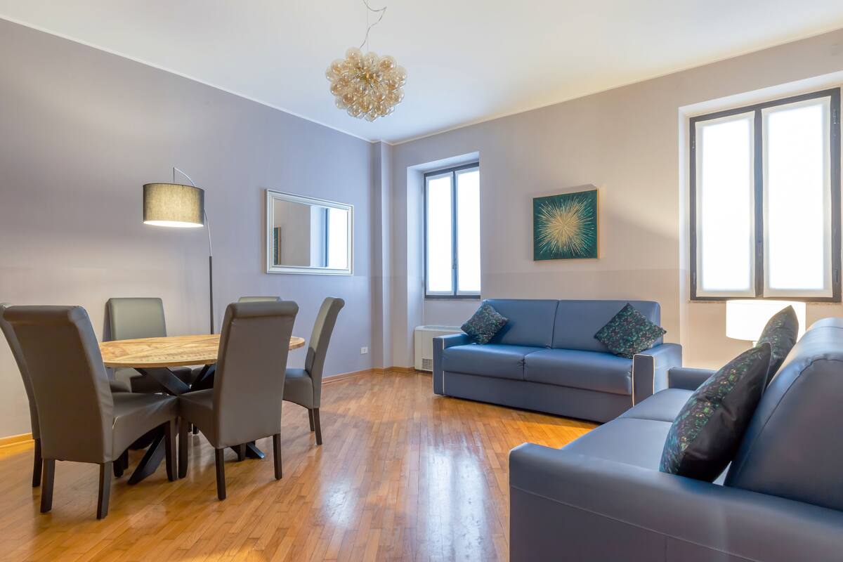 A modern living room with a dining table, chairs, a sofa, and a blue couch.