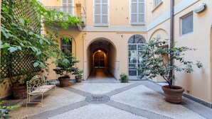Un cortile con una panchina, piante in vaso e un arco centrale che conduce a una porta.