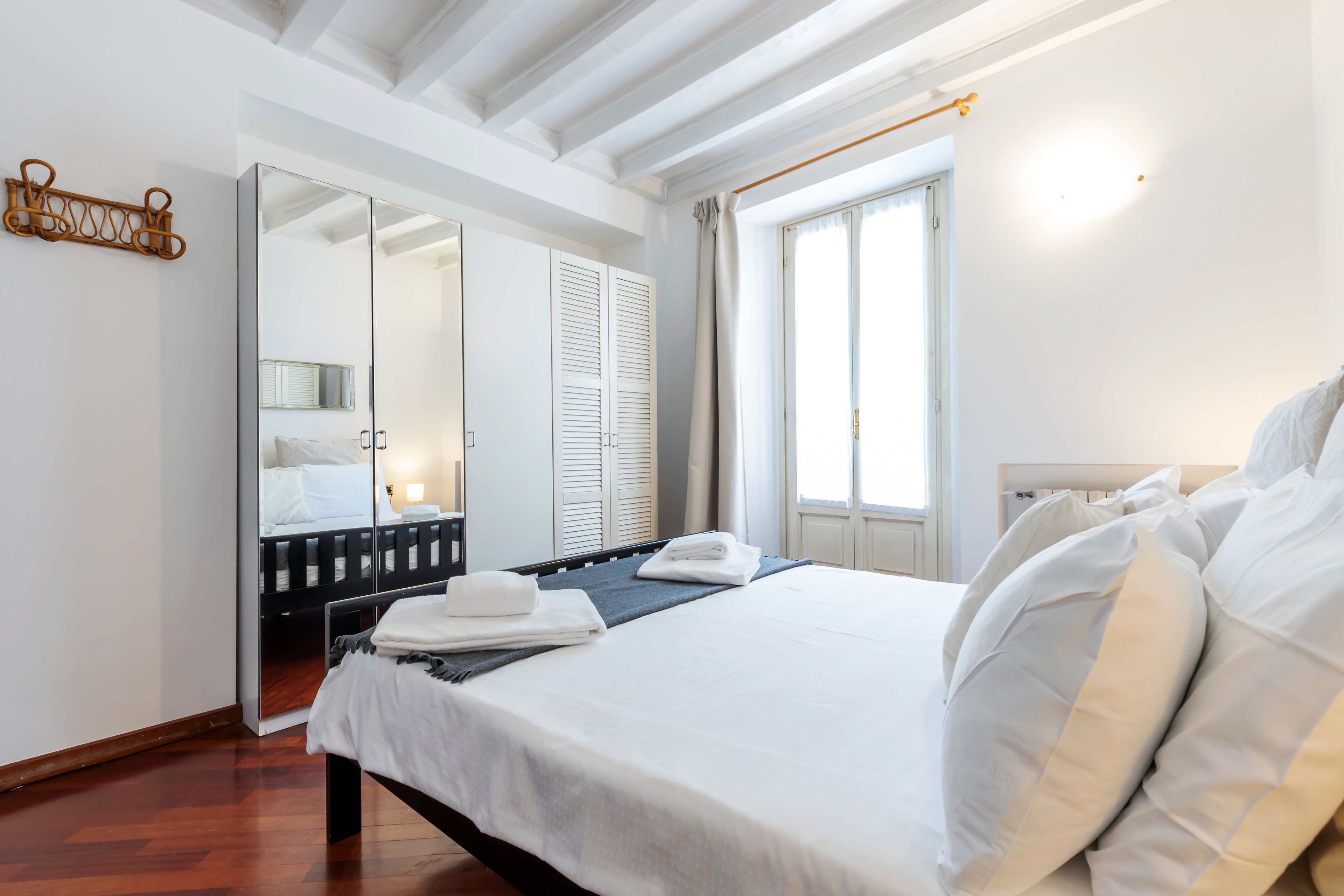 A bedroom with a bed, a large mirror, a wardrobe, and a window with curtains.