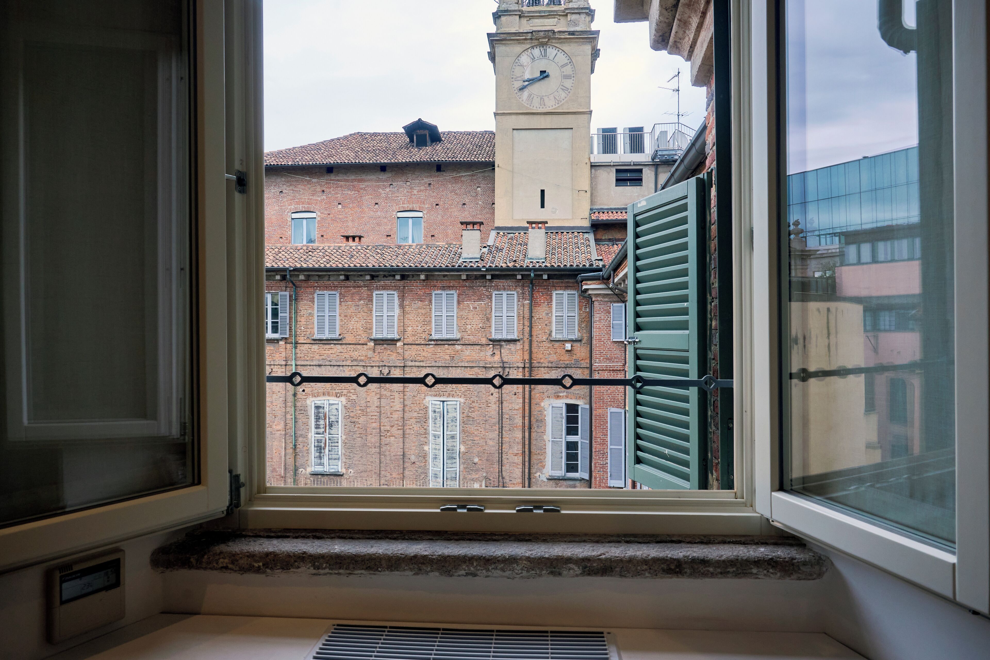 A view from a window with a metal grille, looking out at a building with a clock tower and a brick facade.