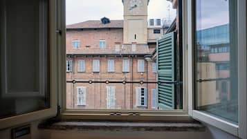 A view from a window with a metal grille, looking out at a building with a clock tower and a brick facade.