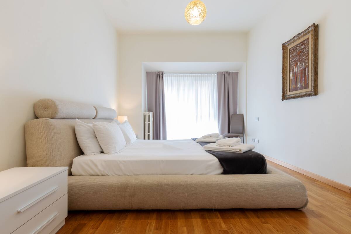 A modern bedroom with a bed, bedside table, and a view of the outside.