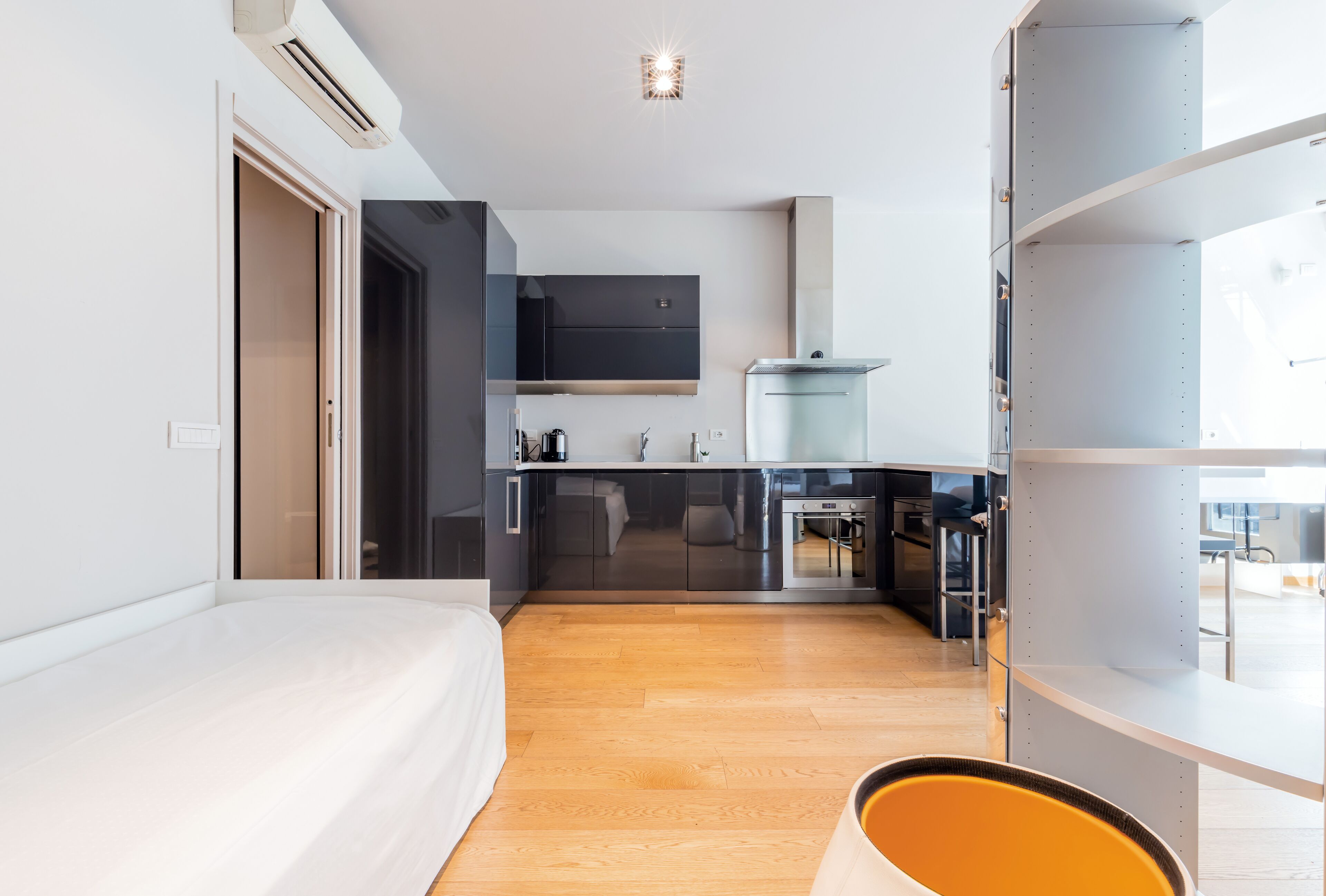 A modern hotel room with a bed, a kitchenette, and a bathroom.