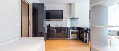 A modern hotel room with a bed, a kitchenette, and a bathroom.
