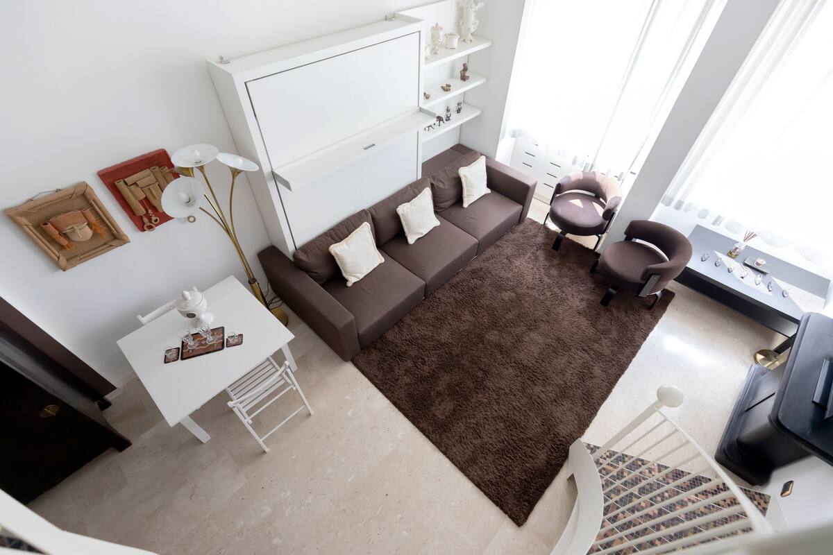 A modern living room with a brown sofa, white side table, and a large window.