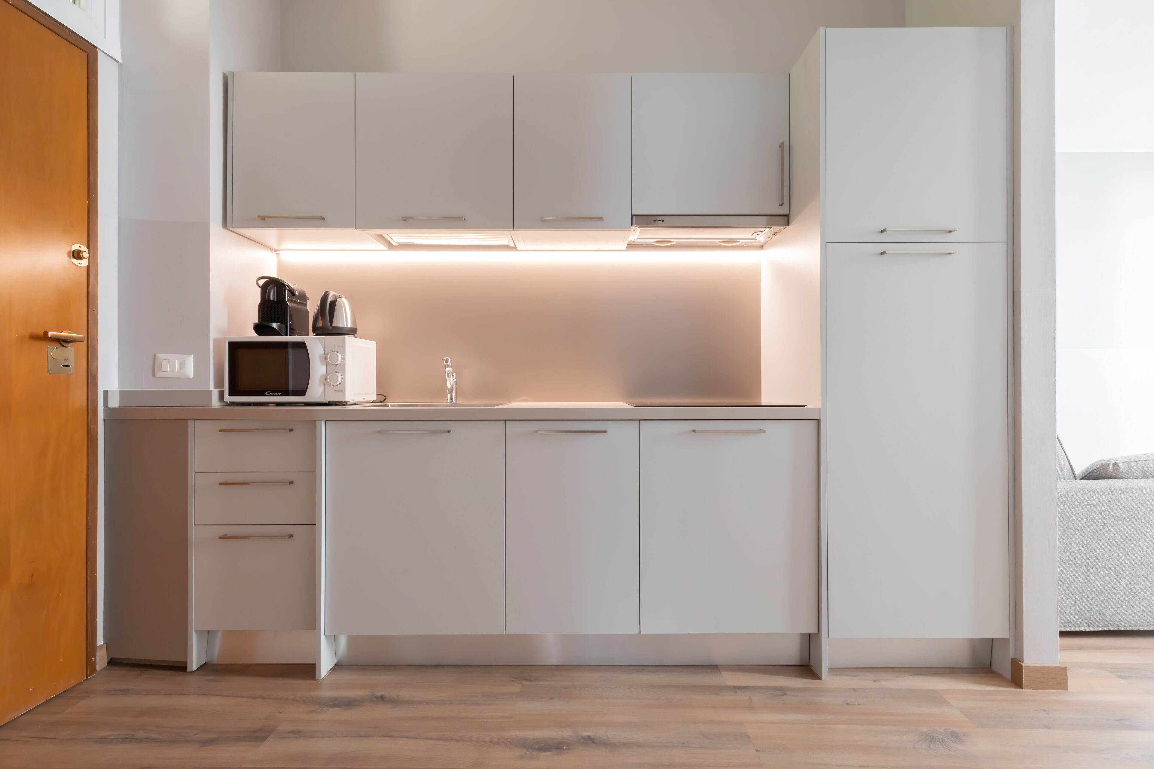A modern kitchen with white cabinets, a microwave, a coffee maker, and a refrigerator.