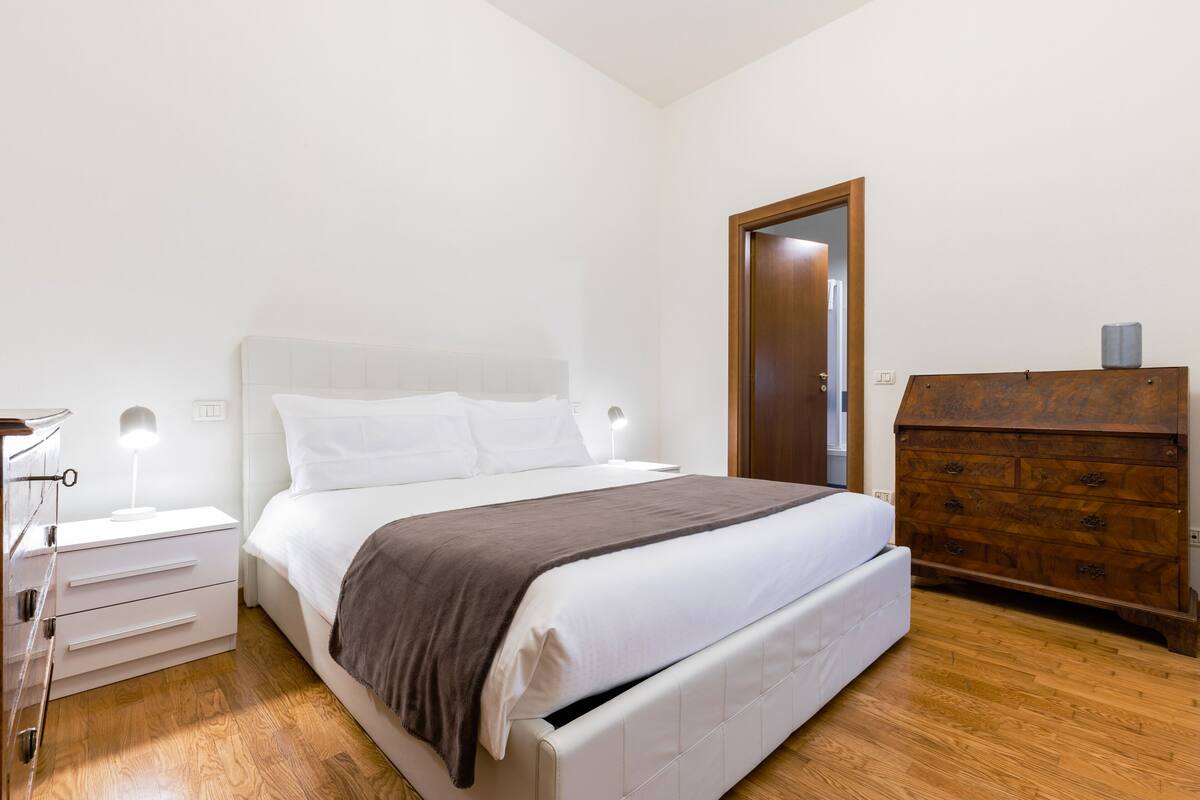 A bedroom with a bed, bedside tables, a dresser, and a door.