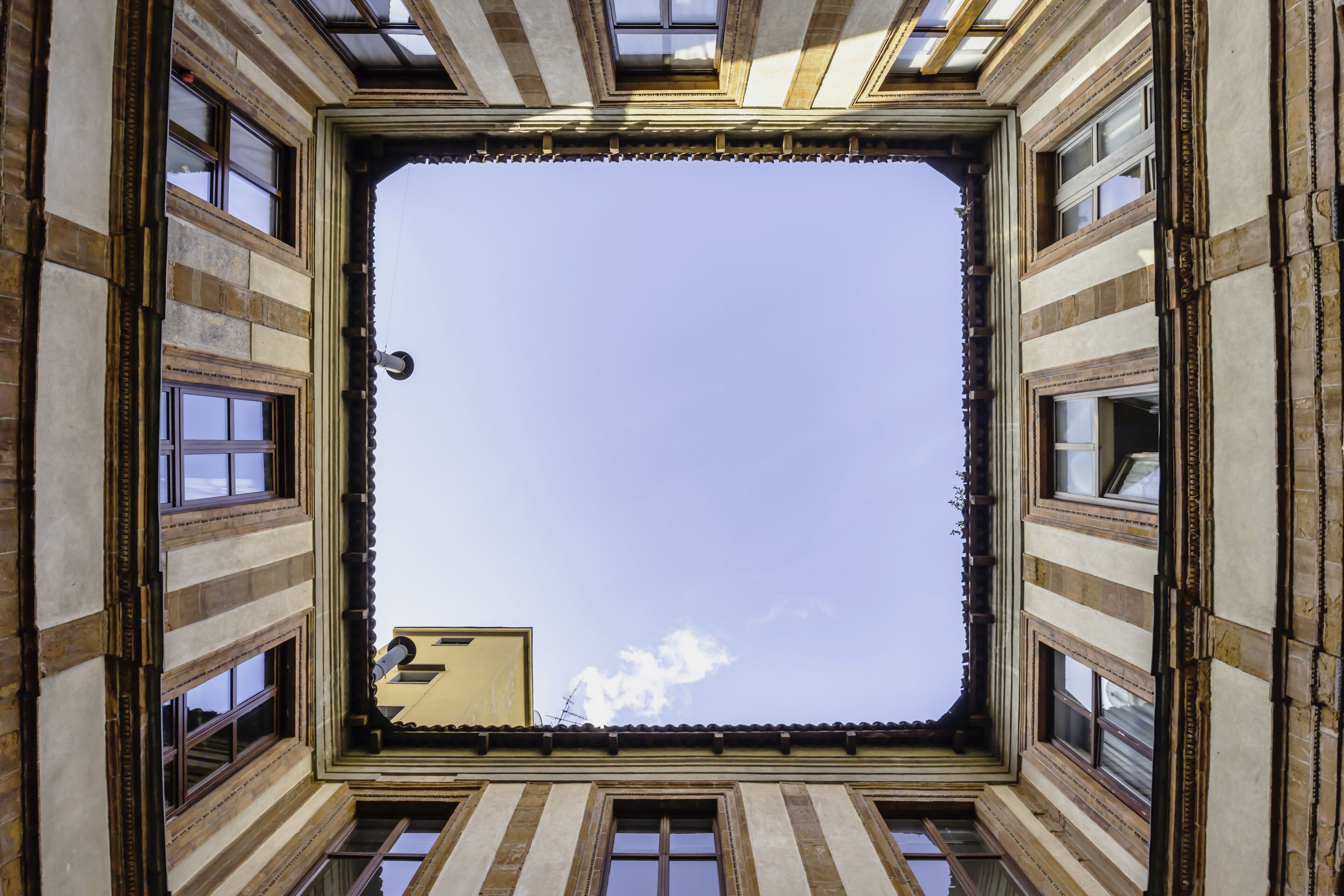 A square skylight with a clear sky view, surrounded by a building with a tiled roof and stone facade.