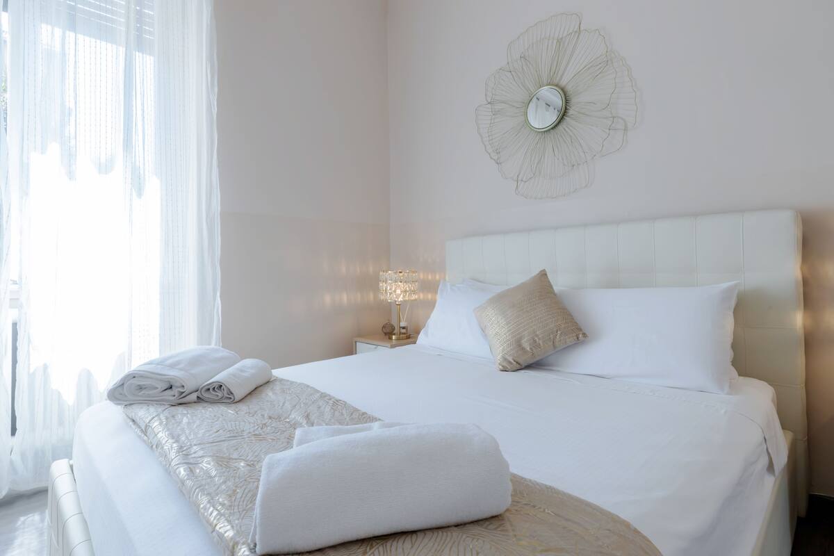 A neatly made bed with white linens and a decorative wall piece above it.