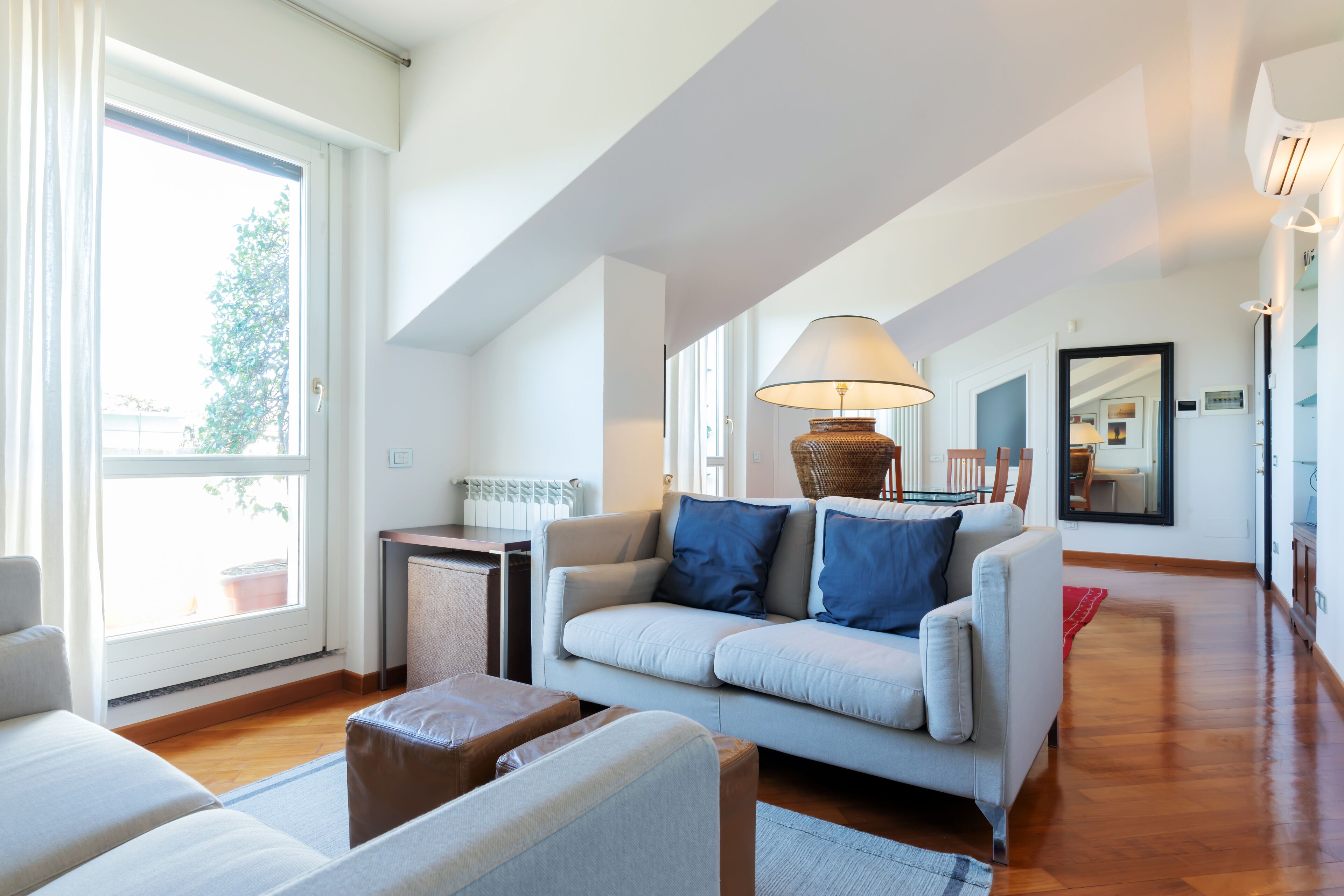 Ein modernes Wohnzimmer mit einer Couch, einer Lampe und Blick ins Freie durch große Fenster.