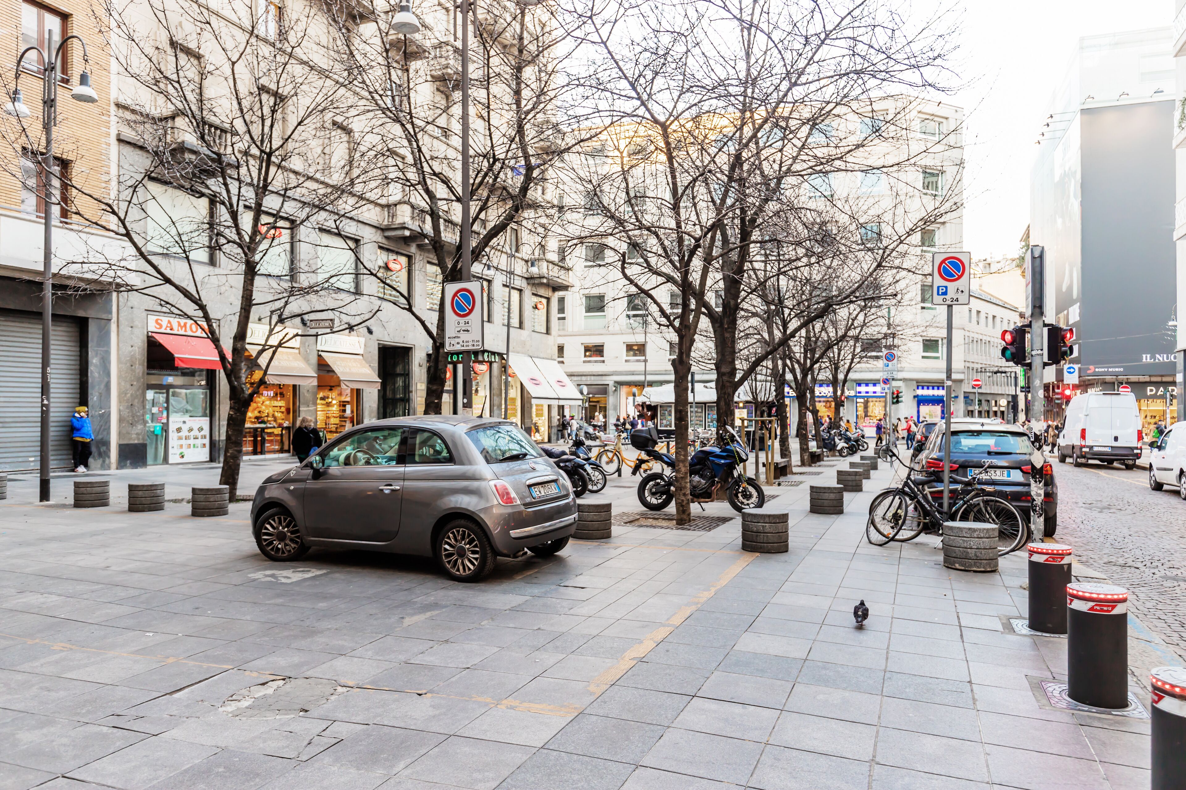 A city street with parked cars, bicycles, and a pedestrian walkway.