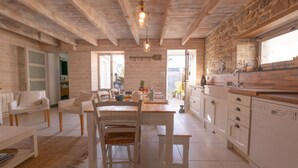 Une cuisine spacieuse avec des meubles blancs, un coin repas doté d’une table et de chaises en bois, et un mur en pierre.