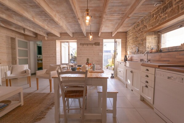 A spacious kitchen with white cabinetry, a dining area with a wooden table and chairs, and a stone wall. - Charming fisherman's cottage in the town centre (Saint-Philibert)