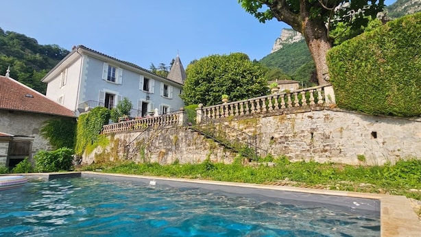 Une piscine avec un mur en pierre et, au fond, un bâtiment dont le toit est recouvert de tuiles.