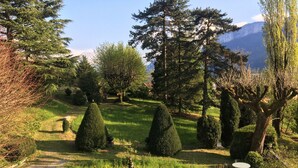 Un jardin avec différents arbres, une statue et une table entourée de chaises.