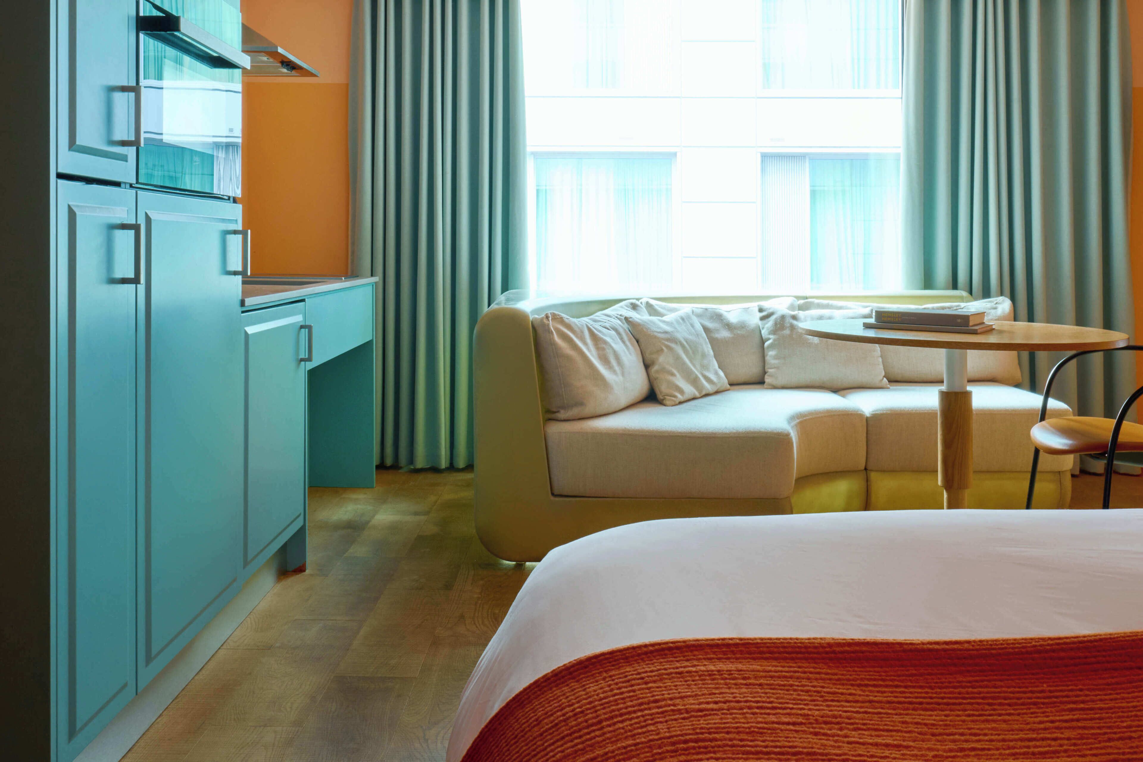 A hotel room with a bed, a sofa, a small table, and a kitchenette.