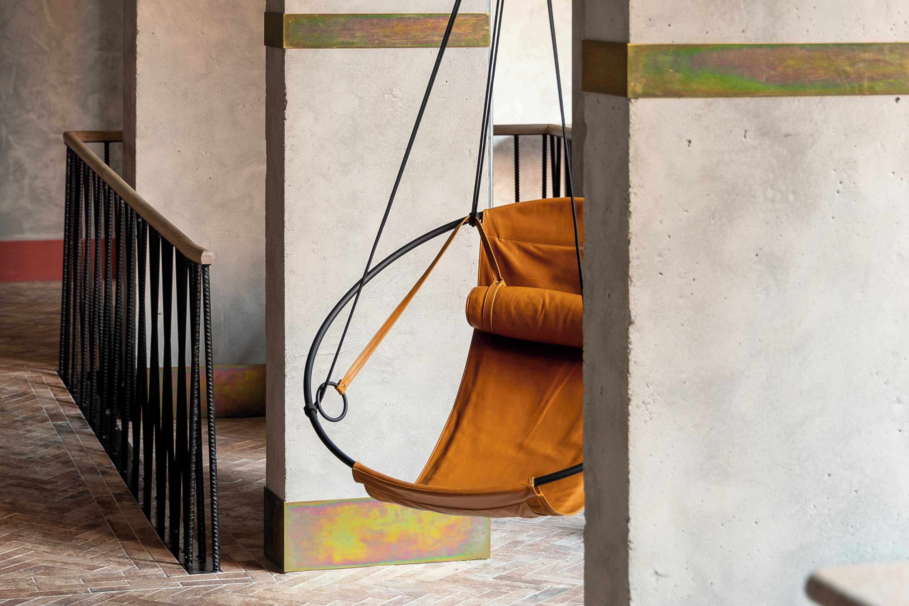 A hanging chair suspended from a ceiling, a metal railing, and a tiled floor.