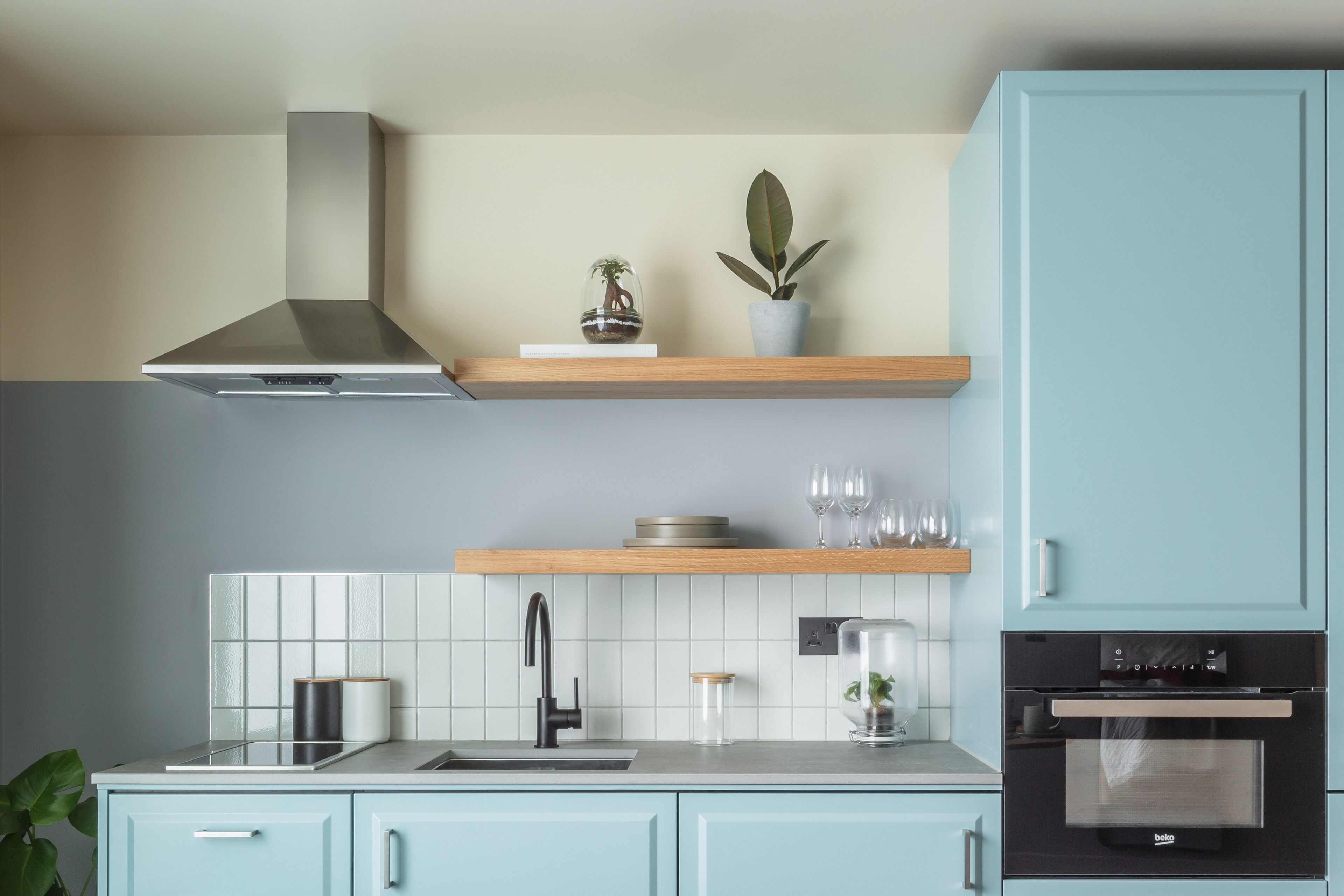 A modern kitchen with a stainless steel range hood, a built-in oven, and a wooden countertop.