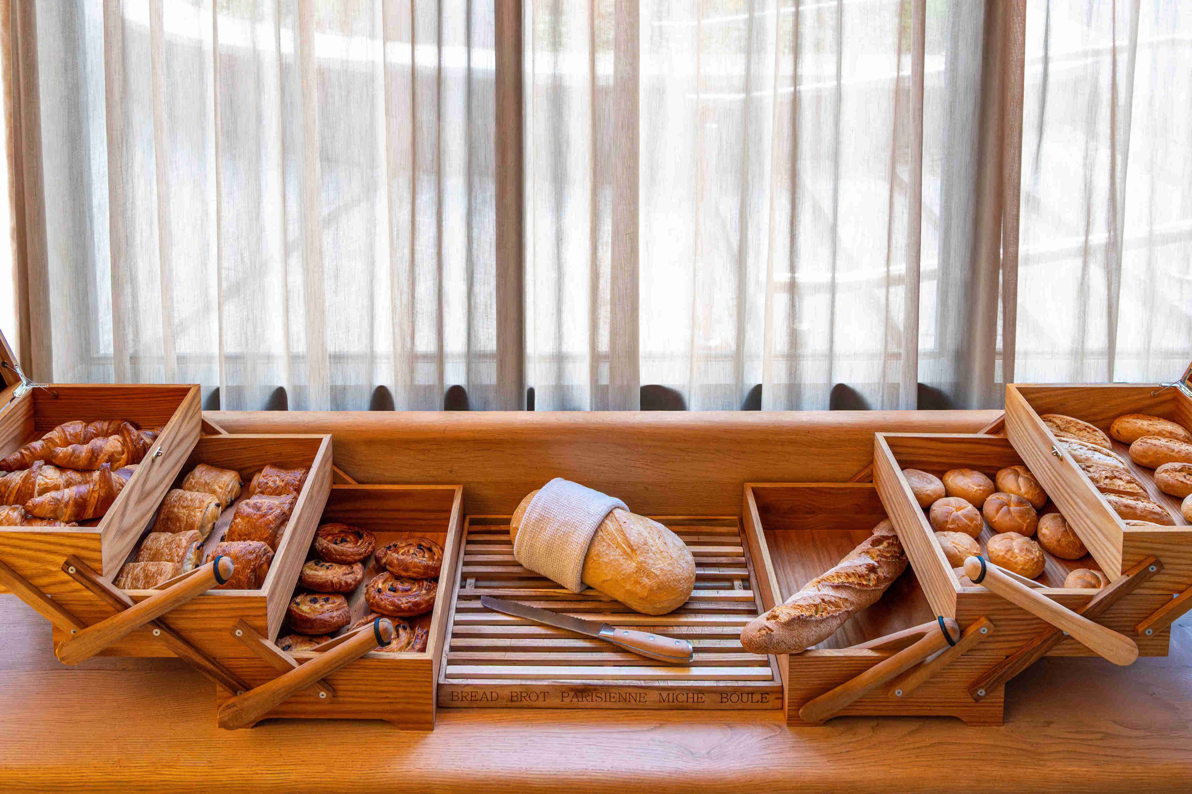 Wooden bread baskets with various baked goods, a knife, and a loaf of bread on a table.