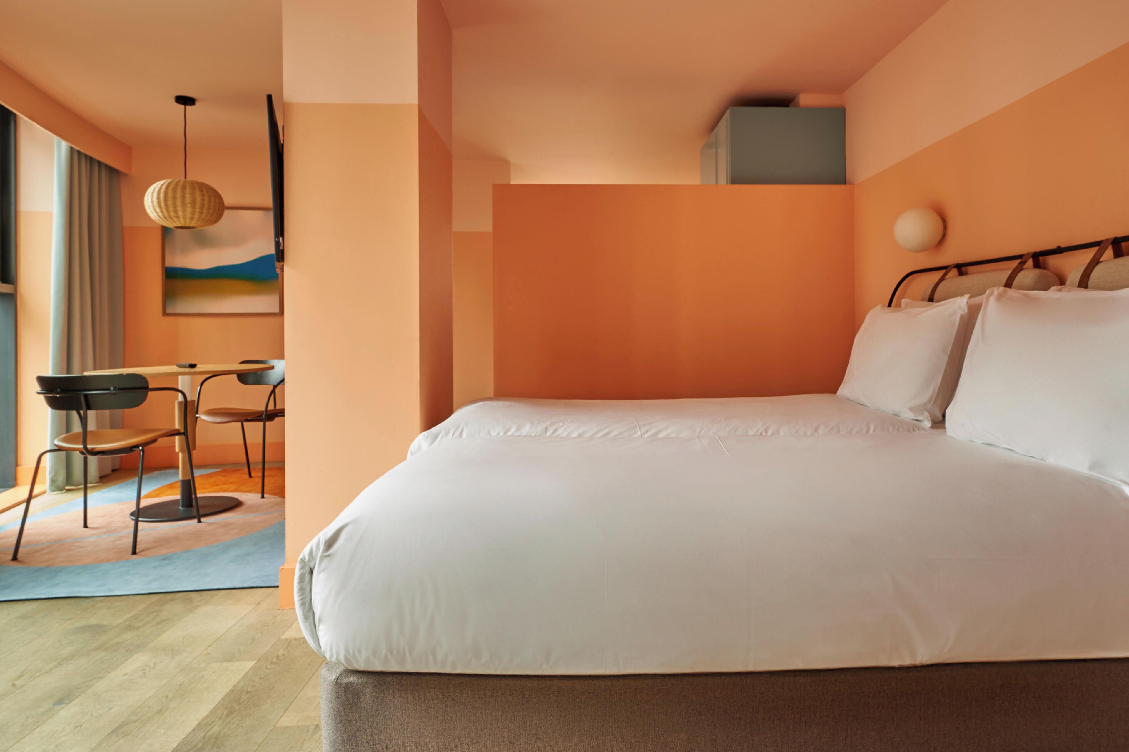 Une chambre avec un grand lit, un bureau avec des chaises, un luminaire suspendu et un tableau accroché au mur.
