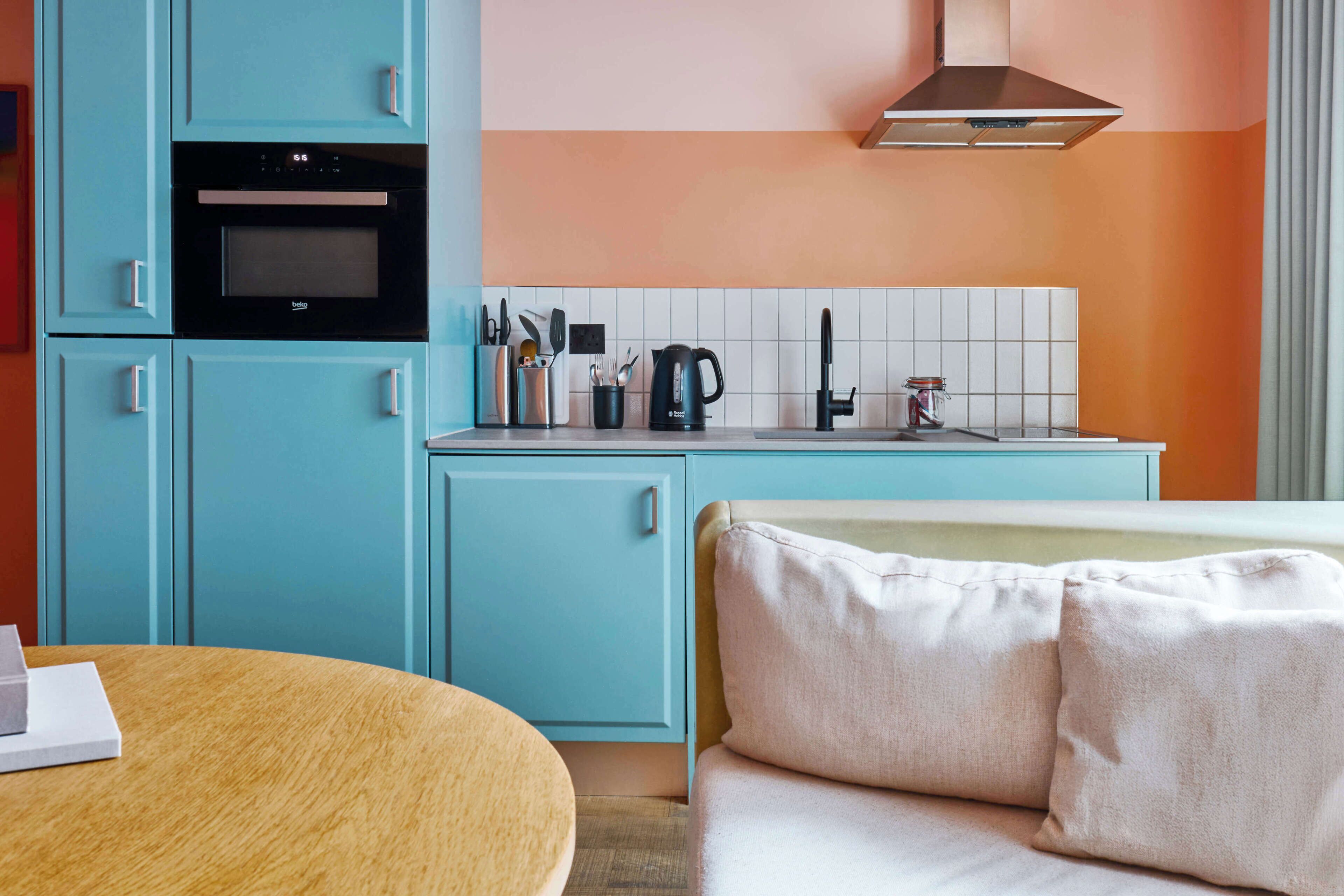 Uma cozinha com armários verde-água, forno preto e painel de azulejos branco.