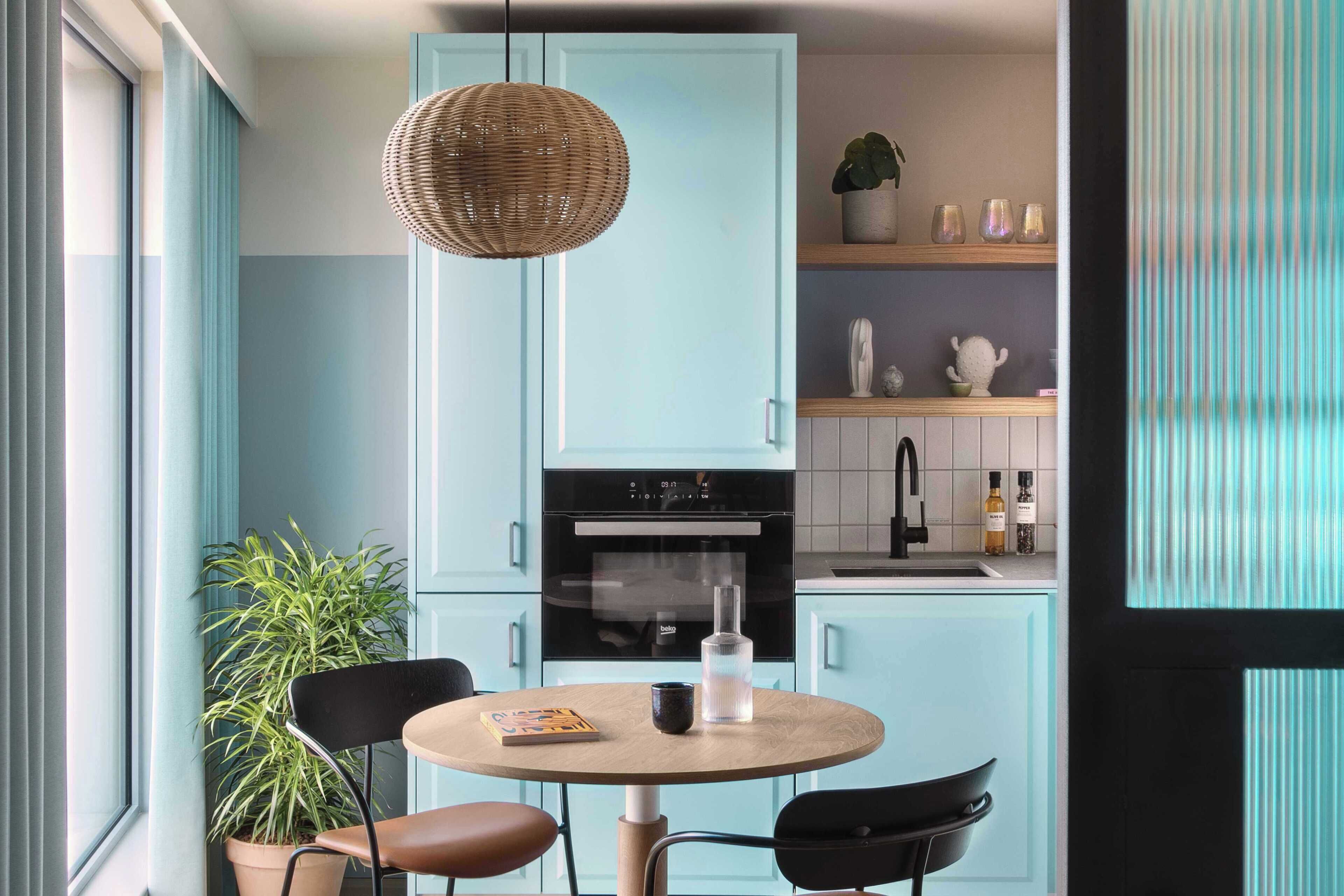 A kitchen with light blue cabinets, a round table with chairs, a hanging light fixture, and a potted plant.
