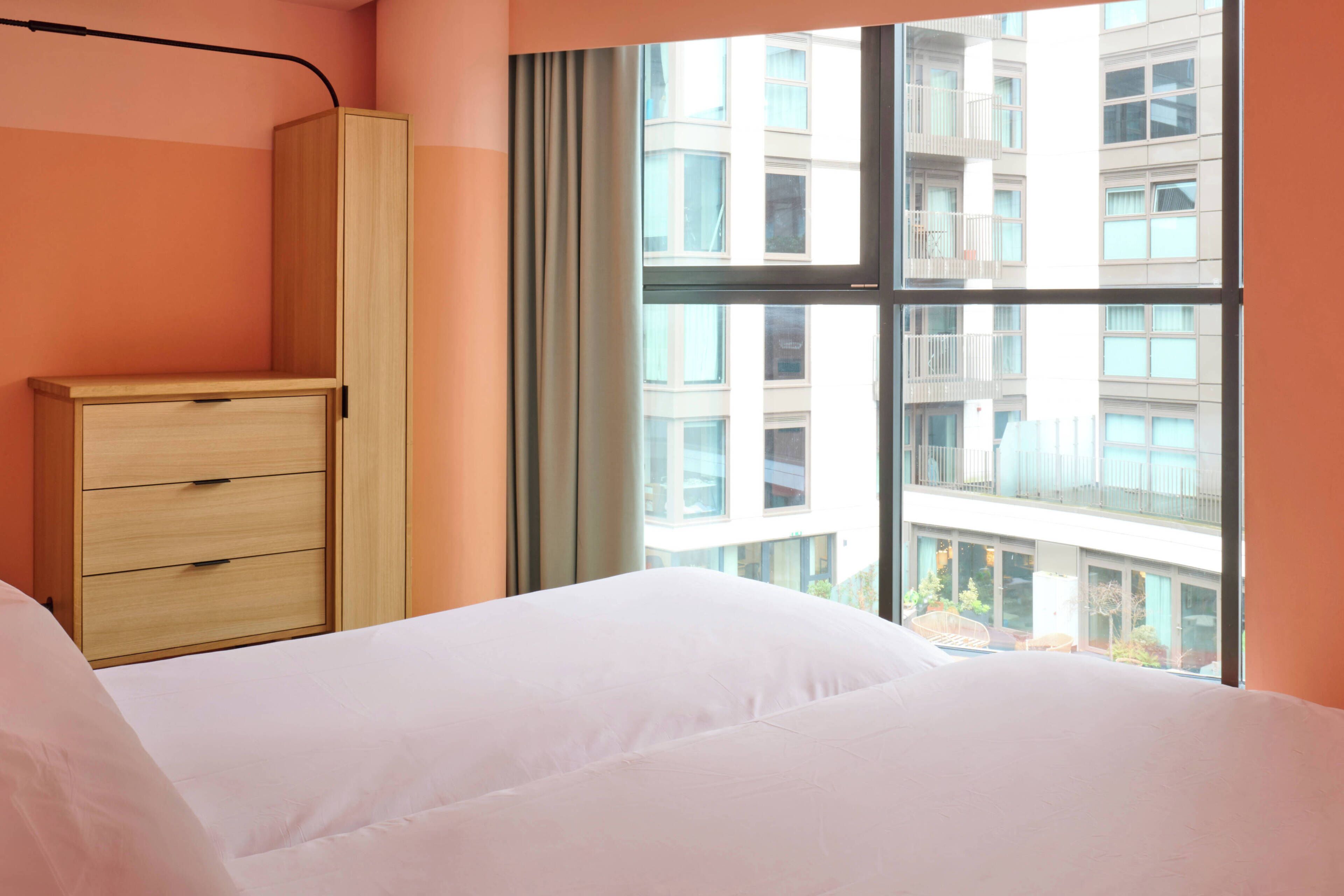 A bedroom with a bed, a wardrobe, and a window with a view of a building.