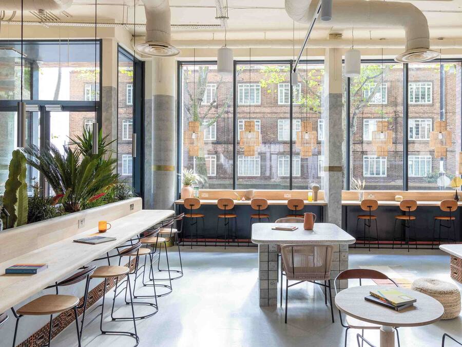 A modern cafe with large windows, bar stools, and a mix of seating arrangements.