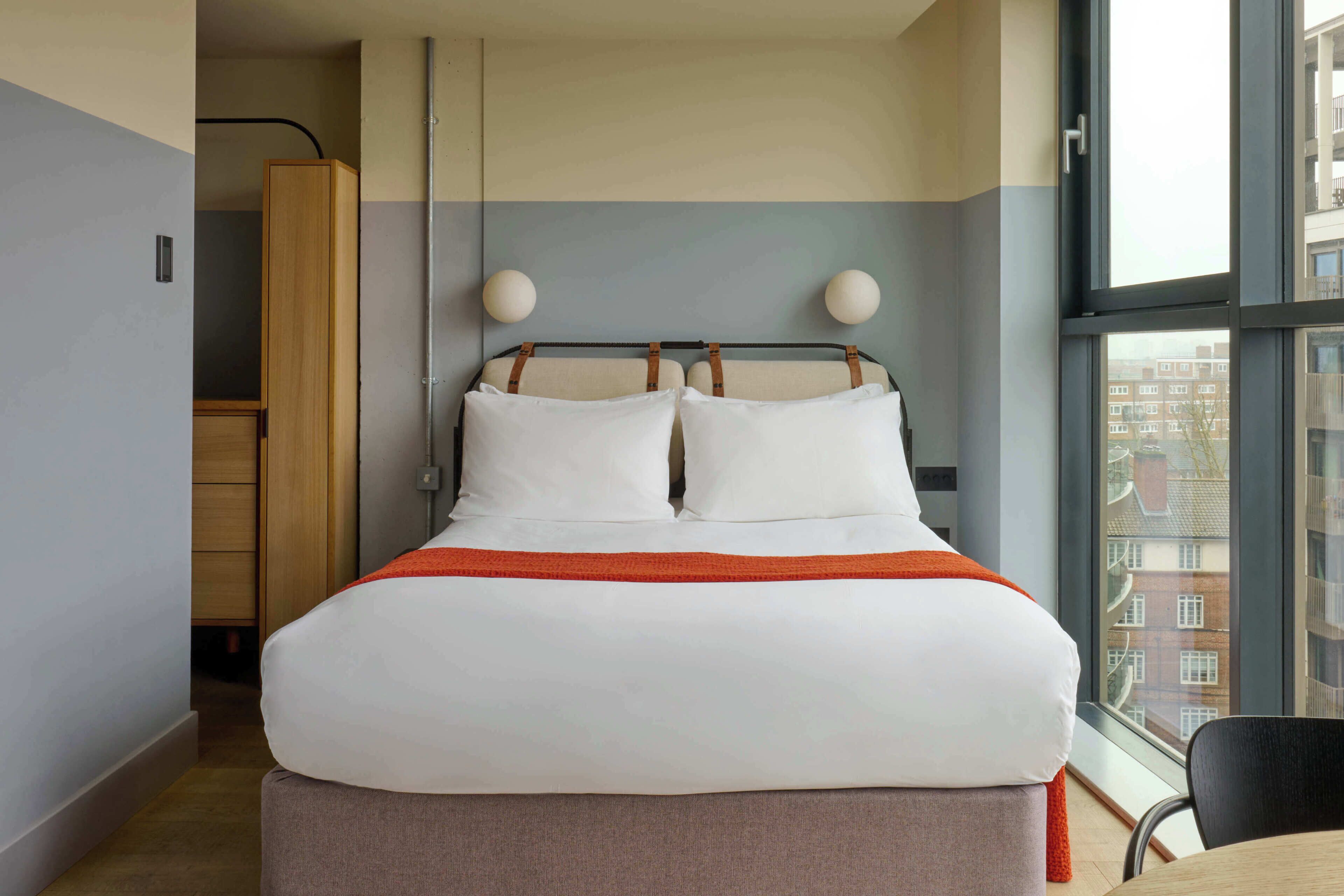 A hotel room with a bed, a window, and a view of buildings.
