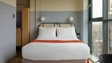A hotel room with a bed, a window, and a view of buildings.