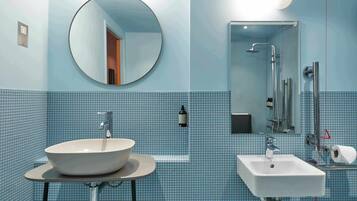 A bathroom with a round mirror, a sink, and a shower area.