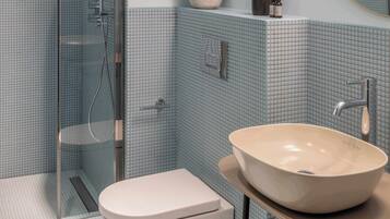 Baño con cabina de ducha de vidrio, inodoro y lavabo sobre encimera.