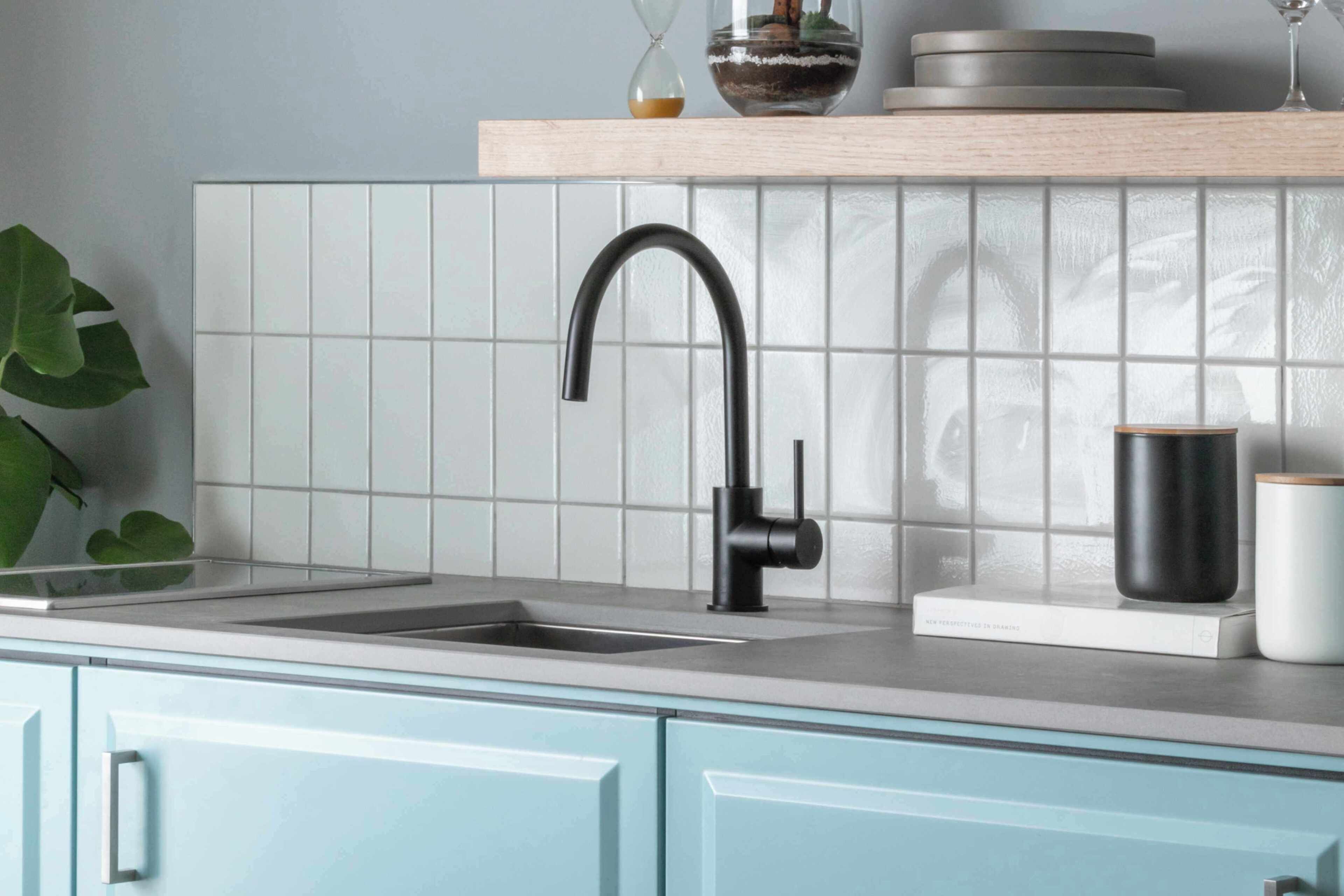 A kitchen with a modern faucet, a sink, a white tiled backsplash, and light blue cabinets.