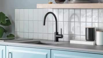 Una cucina con un rubinetto moderno, un lavello, uno schienale piastrellato bianco e mobili azzurri.