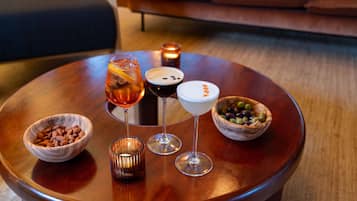 A round wooden table with three glasses of beverages, two bowls of nuts, and a candle.