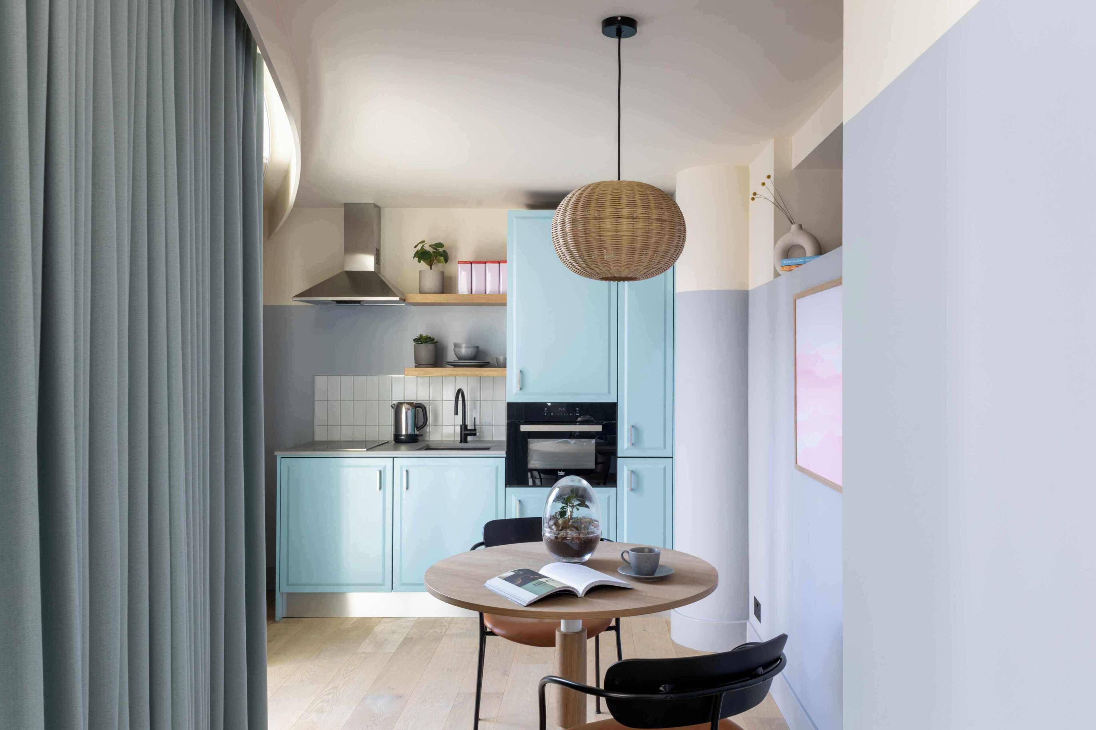 A modern kitchen with light blue cabinets, a round dining table, and a hanging light fixture.