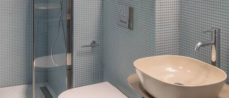 A bathroom with a glass shower enclosure, a white toilet, and a beige sink with a modern faucet.