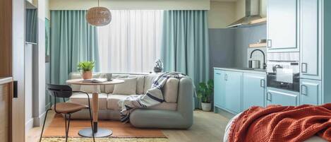 A compact living space with a sofa, a dining table, a kitchen area, and a bed.